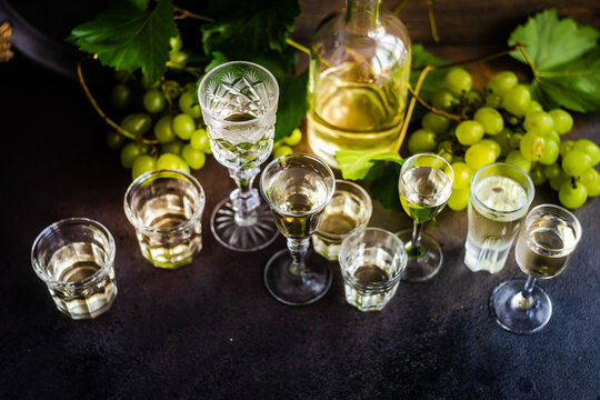 Bottle and assorted glasses of Georgian chacha brandy on a table with bunches of green grapes