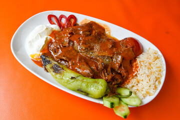 Turkish and Arabic Traditional Ramadan doner kebab with tasty tomato sauce and rice or turkish pilav in white plate on wood table background. ( , Iskender, ekmek arasi pilav ustu doner, doner durum )