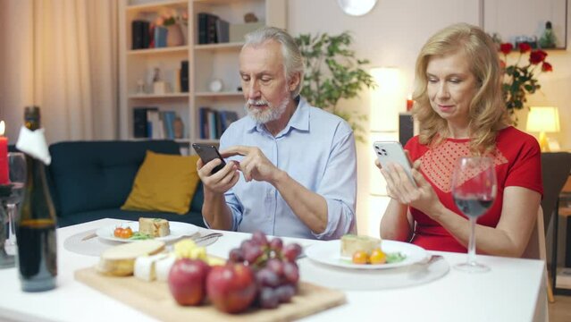 Husband and wife using smartphones instead of talking at romantic dinner
