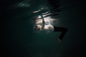 Sink. A young guy in a white shirt falls into the water, a photo from under the water. The concept...