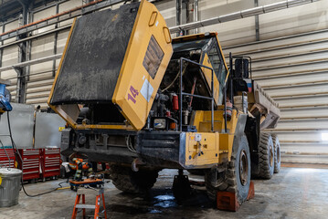 A disassembled articulated dump truck is being repaired in an industrial garage.