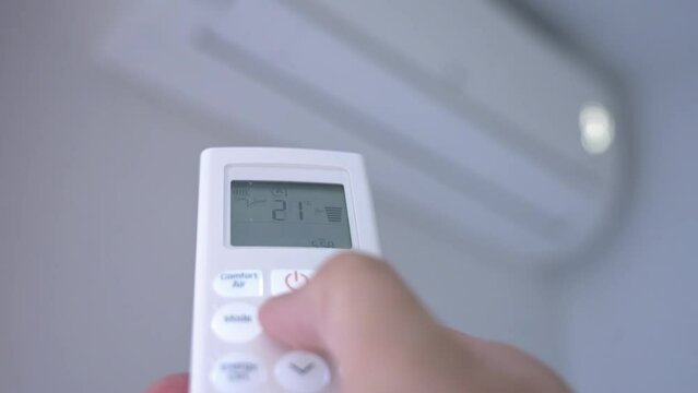 A man's hand pressing the buttons on the control of a split air conditioner to turn it on and set it to the recommended temperature of 25 degrees centigrade