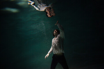 underwater shooting with contrasting light, a guy is swimming underwater, pulling his hand to his...