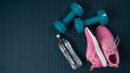 Sports equipment for training in the hall - water, dumbbells and sneakers on the sports mat