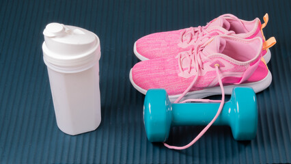 Sneakers, dumbbell and shaker on the mat for training sports background