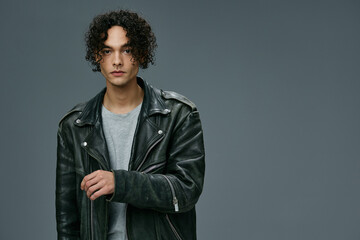 Handsome fashionable stylish tanned curly man leather jacket posing isolated on over gray studio background. Cool fashion offer. Huge Seasonal Sale New Collection concept. Copy space for ad