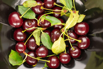 Several sweet juicy cherries on black pottery, close-up, top view.