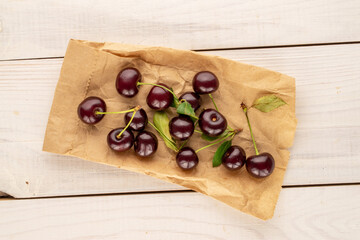 Several sweet juicy cherries with a paper bag on a wooden table, close-up, top view.