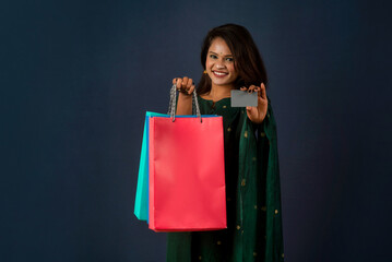 Beautiful young girl or woman holding and posing with shopping bags with credit or debit card on a dark background