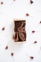 Brown silk ribbon on a roll lies on a white background next to brown seeds pattern