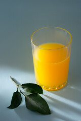 glass of orange juice isolated on light blue background with leaves, soft-focus with space for text, dramatic lighting