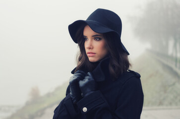 Beautiful woman in black clothes walking outdoors in a mist on autumn day