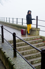 Young elegant woman with suitcase in autumn mist traveling somewhere