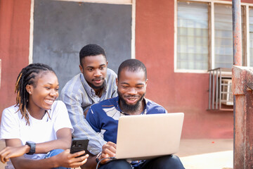 Group of learning millennial african american computer science students at university or college using laptop and mobile phone chatting online