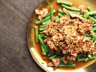 Top view dish of stir fried minced pork, garlic and long bean with red curry paste on wooden background