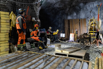 Drillers work in an underground mine on a stationary drilling machine.
