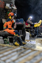 Drillers work in an underground mine on a stationary drilling machine.