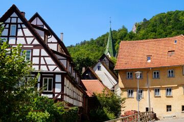 old timber-framed houses on the River Blau (or Blue River) near the turquois pond called Blautopf (Blue Pot) and beautiful old Blaubeuren Abbey in the background (Blaubeuren, Germany)	