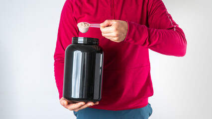 A man in a sports jacket with a can of sports nutrition puts protein into the measuring spoon