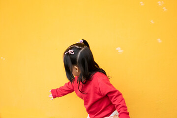 Little girl chase bubbles. She is isolated in a yellow background and wears a red sweater