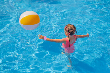 A girl in a pink swimsuit runs after an inflatable ball in the swimming pool. Water games at the...