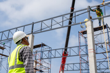 A construction engineer inspects the installation of a factory roof steel frame that uses a mobile crane to lift it up to a height.