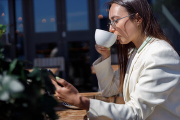 Attractive business woman in sunglasses drinking coffee and using phone sitting in cafe