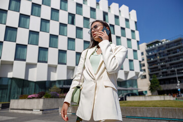 Attractive young businesswoman in white suit talking phone standing near business centre