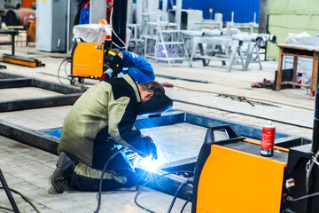 Fototapeta premium An electric welder works at an industrial enterprise. The process of welding a metal structure from a metal profile. Unrecognizable person. Foreground