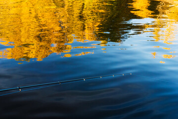Fototapeta na wymiar Summer fishing for predatory fish. Fragment of spinning on the background of water and reflection of yellow trees. Close-up