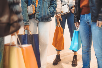Detail of young trendy people holding paper shopping bags standing in front of a window shop at the...