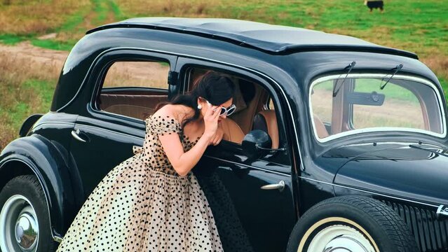 Fantasy portrait elegant happy retro lady woman driver stopped on road resting, wearing vintage sunglasses. Luxurious puffy midi white dress with black polka dots. Red lips makeup, girl smiling face