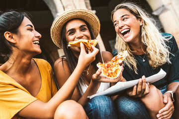 Happy friends eating street food on summer vacation - Three women eating pizza slice on city street...