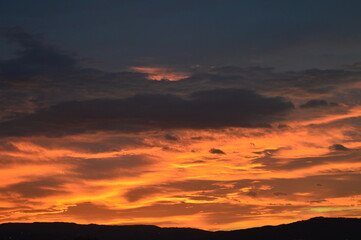 A beautiful sunset behind the mountain, golden light spreading across the horizon and illuminating the clouds