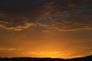 A beautiful sunset behind the mountain, golden light spreading across the horizon and illuminating the clouds