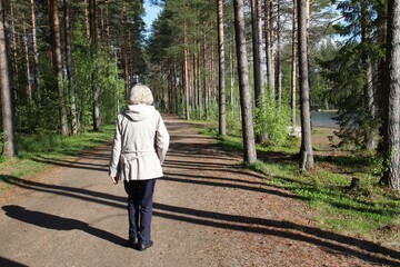 An elderly lady is taking a walk in the nature and enjoying the sunshine. 