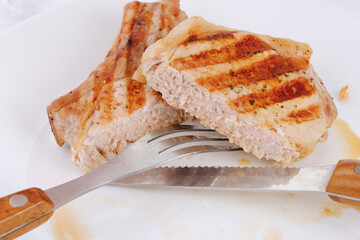 Cut in two pork steak on a white plate with a knife and fork. Close-up, macro.