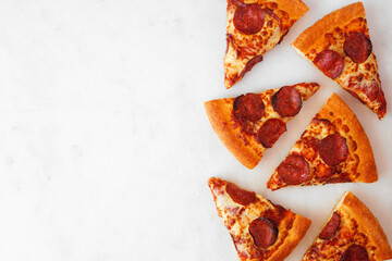 Pepperoni pizza slice side border. Top view over a white marble background. Copy space.
