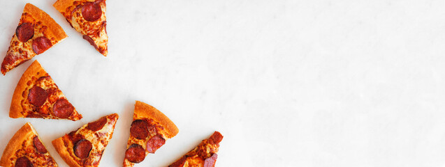 Pepperoni pizza slice corner border. Above view over a white marble banner background. Copy space.