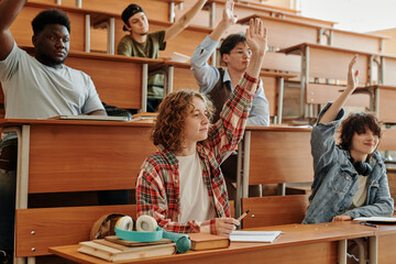 Several youthful interracial students raising hands to ask questions to teacher about new subject...