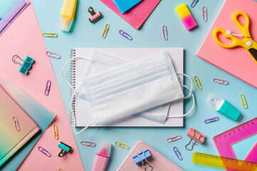 Protective medical mask on creative student desk with colorful modern school supplies on blue and...