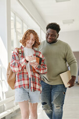 Two teenage classmates in casualwear discussing curious stuff in smartphone held by cute smiling girl after lessons