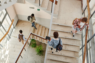 Overview of teenage students going up and down staircase in corridor while leaving for home or...