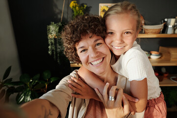 Happy young brunette woman with dark short curly hair and her youthful daughter looking at camera...