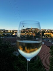 Obraz premium A glass of Georgian wine framing a wonderful cathedral during sunset in Tbilisi, Georgia