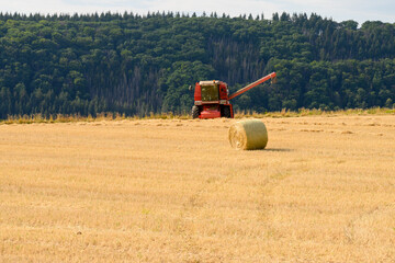 Obraz premium Front view of a combine harvester without header in a golden field with bale