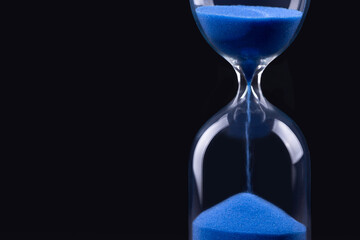 Hourglass with blue sand on black background
