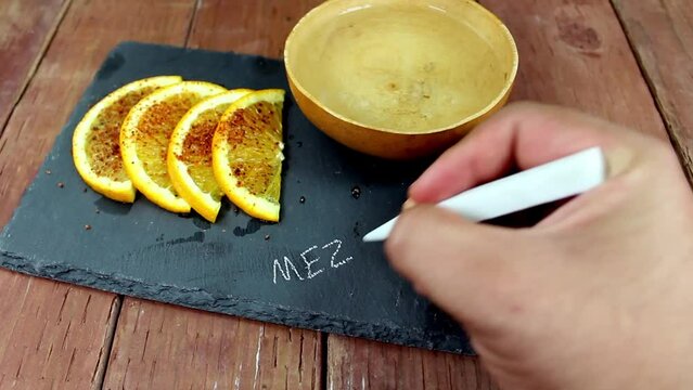 hand writing the word MEZCAL on a stone plate with a jicara bowl of mezcal