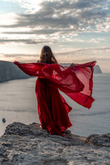 A woman in a red dress stands above a stormy sky, her dress fluttering, the fabric flying in the...