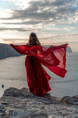 A woman in a red dress stands above a stormy sky, her dress fluttering, the fabric flying in the wind.